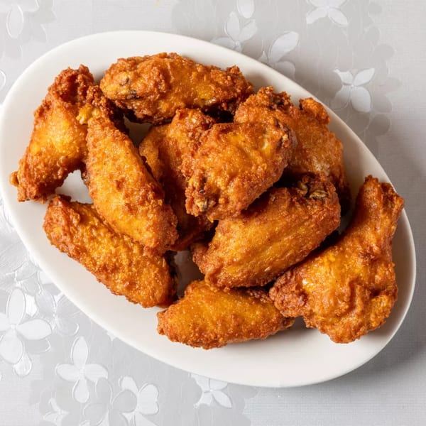 A white oval platter filled with golden-brown, crispy fried chicken wings on a white floral tablecloth.