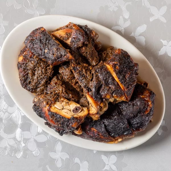 A white oval platter filled with dark, richly spiced Indian chicken pieces on a floral tablecloth.