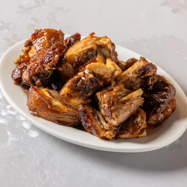 A white oval plate filled with glistening, dark brown pieces of Indian-style grilled meat.